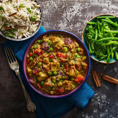 Slimming World food range mushy pea curry in purple bowl on a grey table with rice and green beans on the side